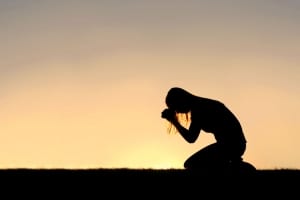 Silhouette of a woman on her knees praying-stress management