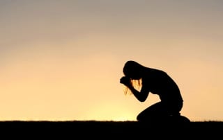 Silhouette of a woman on her knees praying-stress management