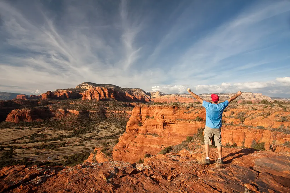 Man standing on a Sedona vortex red rock vista with arms raised in a gesture of freedom and healing.
