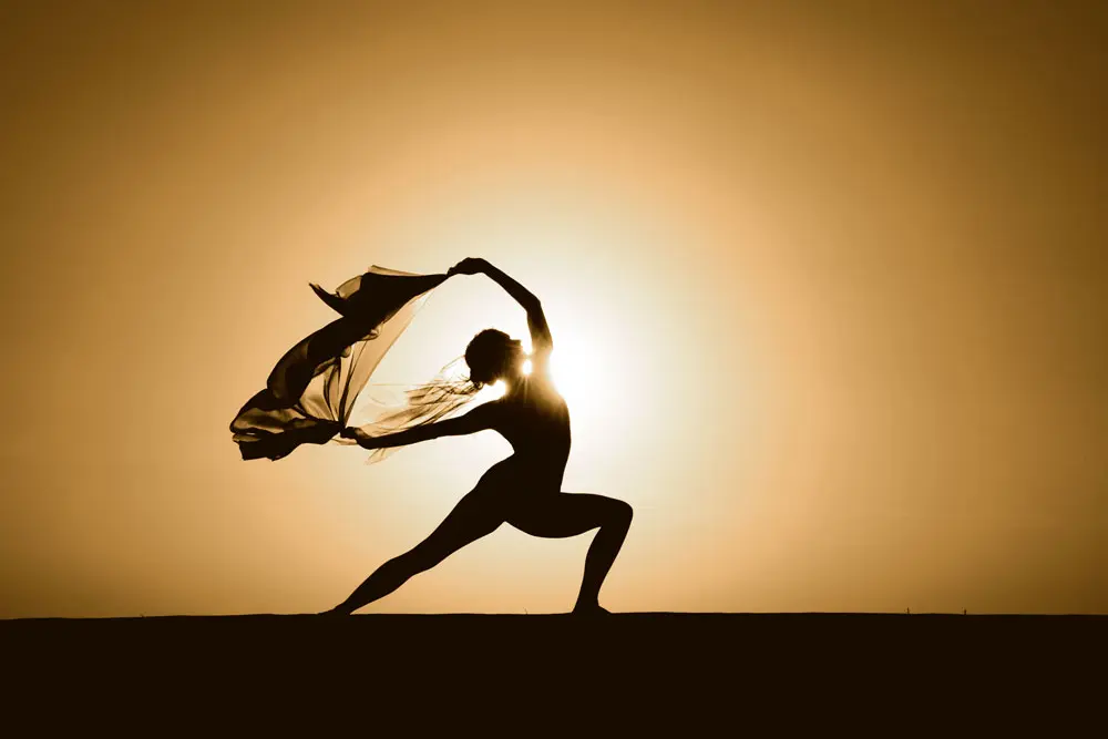 Silhouette of a person performing a deep yoga lunge or runner's stretch against a warm, glowing amber background.