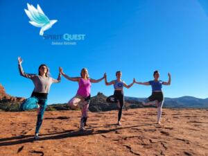 Group of women practicing outdoor yoga on a Sedona red rock ledge with Cathedral Rock in the background.