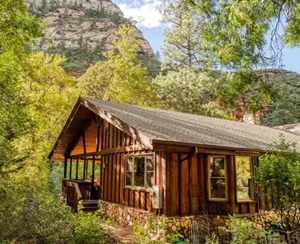 Exterior view of a rustic, cozy wooden cabin with a small deck and stairs leading up to the entrance.