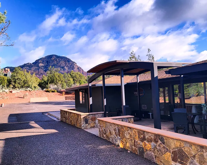 spiritquest-sedona-retreats-retreat-center Exterior view of the SpiritQuest Sedona Retreat Center sanctuary building with a red rock mountain backdrop under a blue sky.