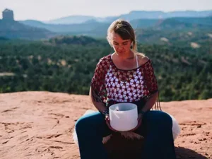 Woman on redrocks overlooking Sedona, AZ as she plays a crystal healing bowl.