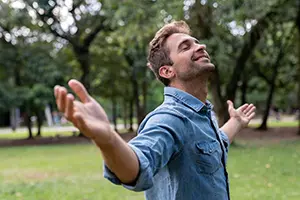 A cheerful man smiling and looking up with open arms during an outdoor men's retreat session.